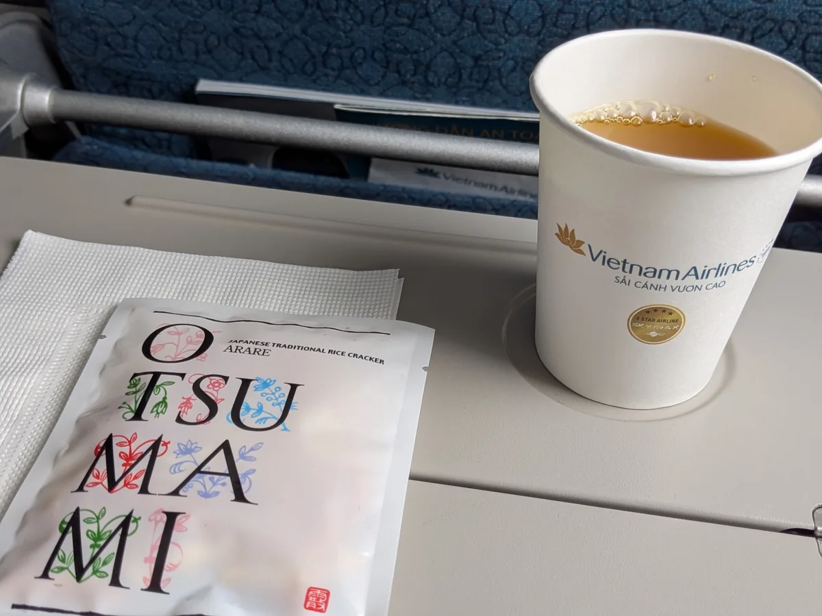 ベトナム航空のロゴ入り紙コップのお茶とあられのおつまみ