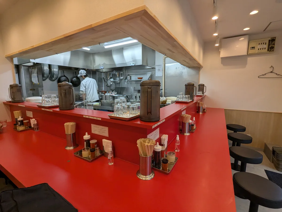 荒畑の店内。赤いL字カウンター9席と、厨房が見えるオープンな造り
