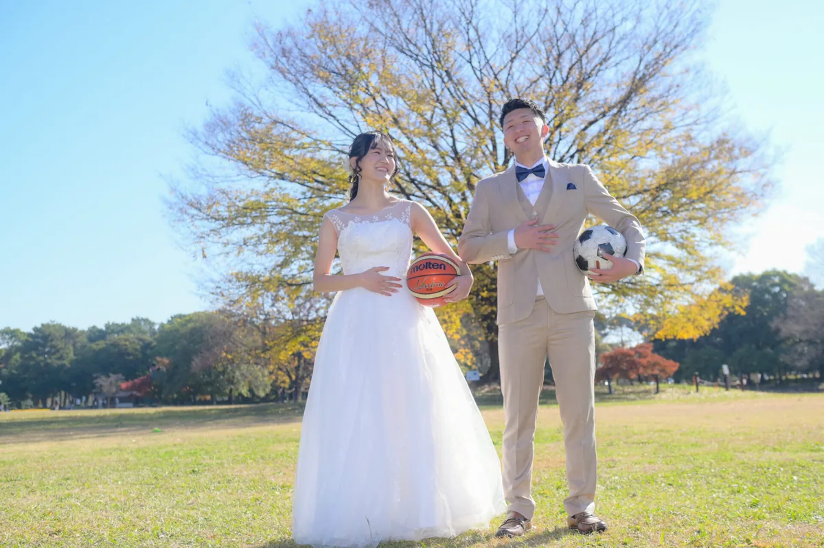 黄葉した公園でバスケットボールとサッカーボールを持ち笑顔で撮影するウェディングフォト