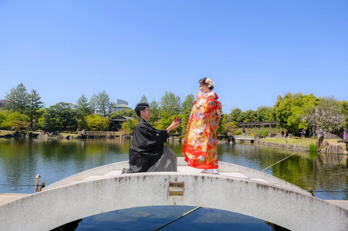 日本庭園の石橋の上で新郎がひざまずきプロポーズする色打掛の和装ロケーションフォト