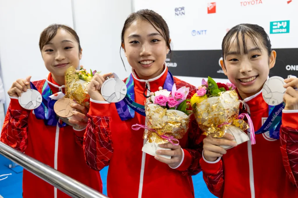左から岡村真選手、岸里奈選手、中村遥香選手。体操女子団体 銀メダルの3人がメダルと花束を手に笑顔
