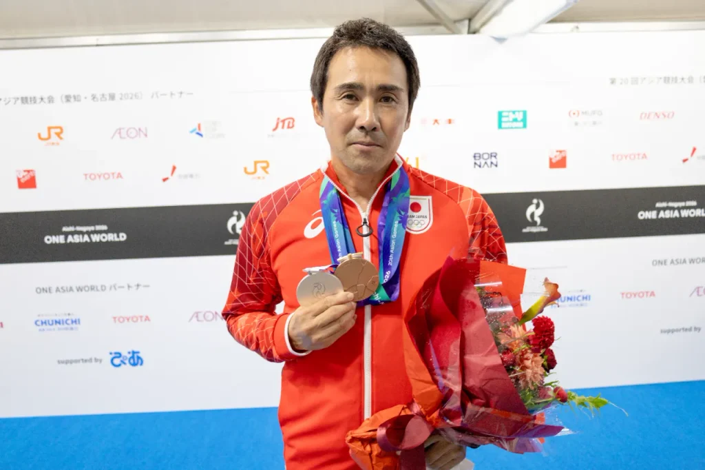 総合馬術の団体銀メダルと個人銅メダルを胸に、花束を手にする大岩義明選手