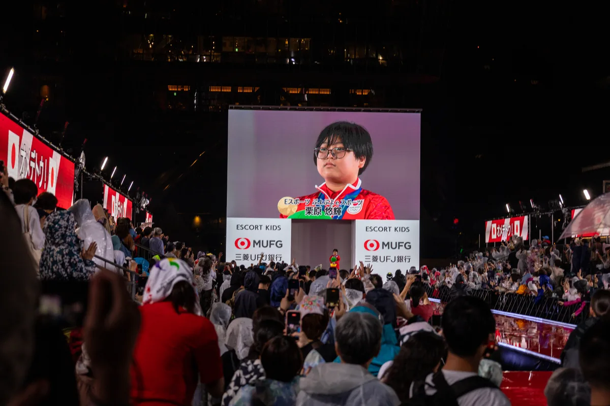 メダリストセレブレーションのステージで大型ビジョンに映し出されたぷよぷよeスポーツ金メダルの栗原悠輝選手と、雨の中で見守る観客