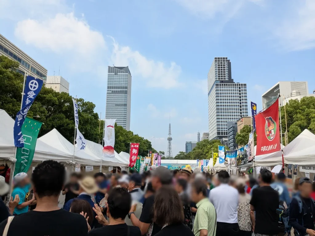 ふるさと全国県人会まつり2026の会場。県人会ののぼりが並ぶテントの通りを埋める来場者と名古屋テレビ塔