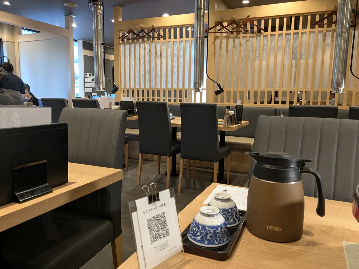 丸明 茶屋ヶ坂店の店内。木目のテーブルとグレーのソファー席が並ぶ広い客席