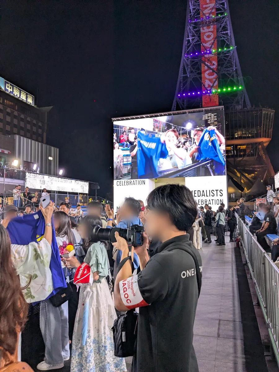 大型ビジョンに映るメダリストを立見エリアからスマートフォンで撮影する観客