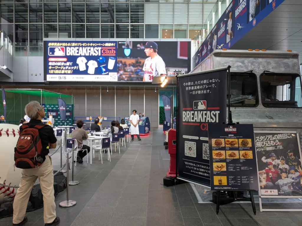 JRゲートタワー1階のMLB Breakfast Club会場。大型ビジョンのMLB中継とフードトラック、観戦席が並ぶ