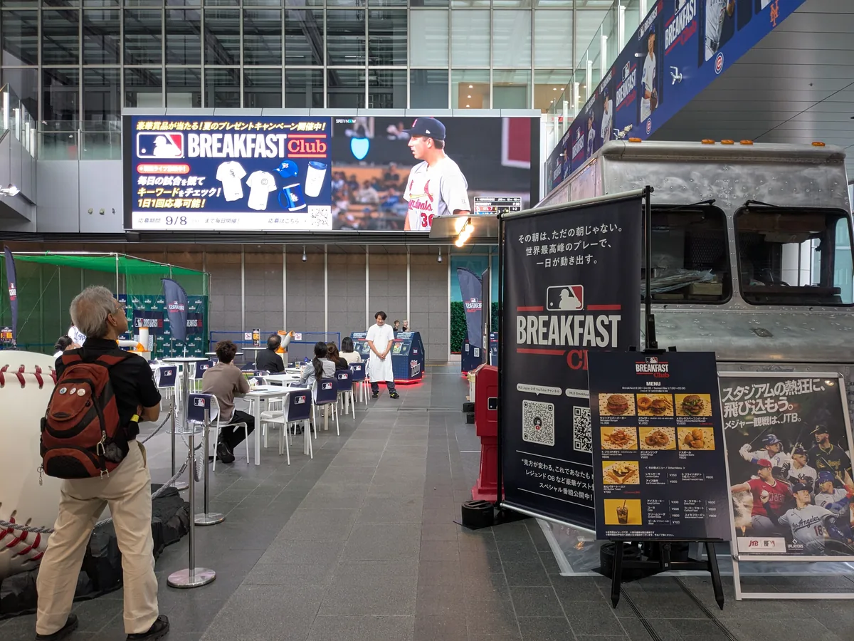 JRゲートタワー1階のMLB Breakfast Club会場。大型ビジョンのMLB中継とフードトラック、観戦席が並ぶ