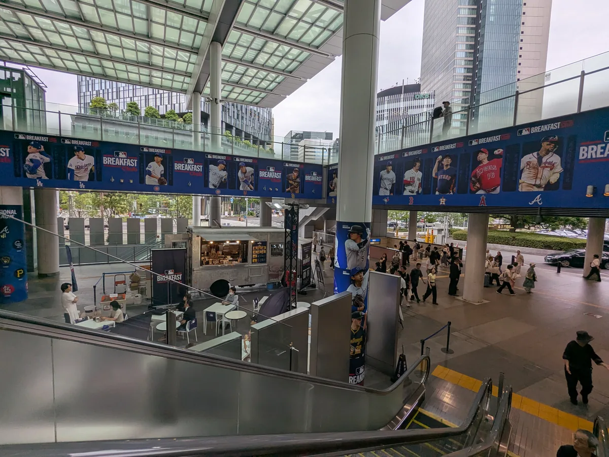 エスカレーターから見下ろしたJRゲートタワー1階のMLB Breakfast Club会場全景。MLB選手のバナーとフードトラック