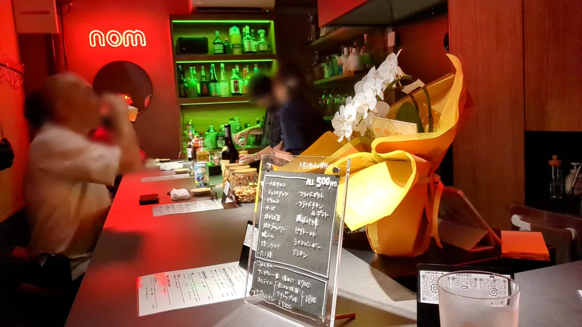 nomのネオンサインと緑に光る酒棚が見える名駅のバーnomのカウンター席