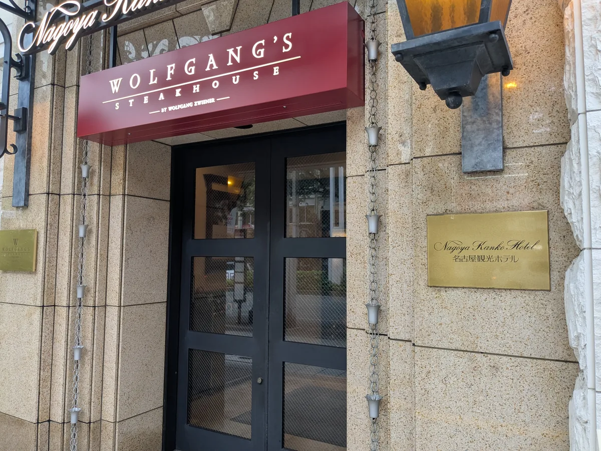 名古屋観光ホテル正面玄関に掲げられたウルフギャング・ステーキハウスのワインレッドの看板と名古屋観光ホテルの金色の銘板