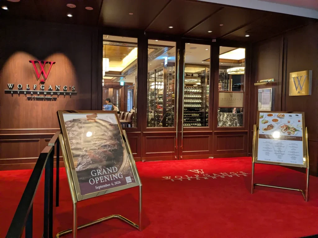 ウルフギャング・ステーキハウス名古屋店の館内入口。赤いカーペットにWのロゴ、GRAND OPENINGの立て看板とガラス張りのワインセラー