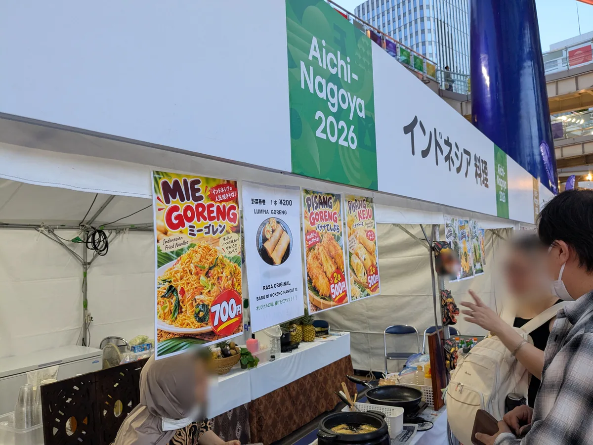 アジアパラ ライブサイトのインドネシア料理ブース。ミーゴレン700円、野菜春巻1本200円、ピサンゴレン2本500円などのメニューが掲示されている