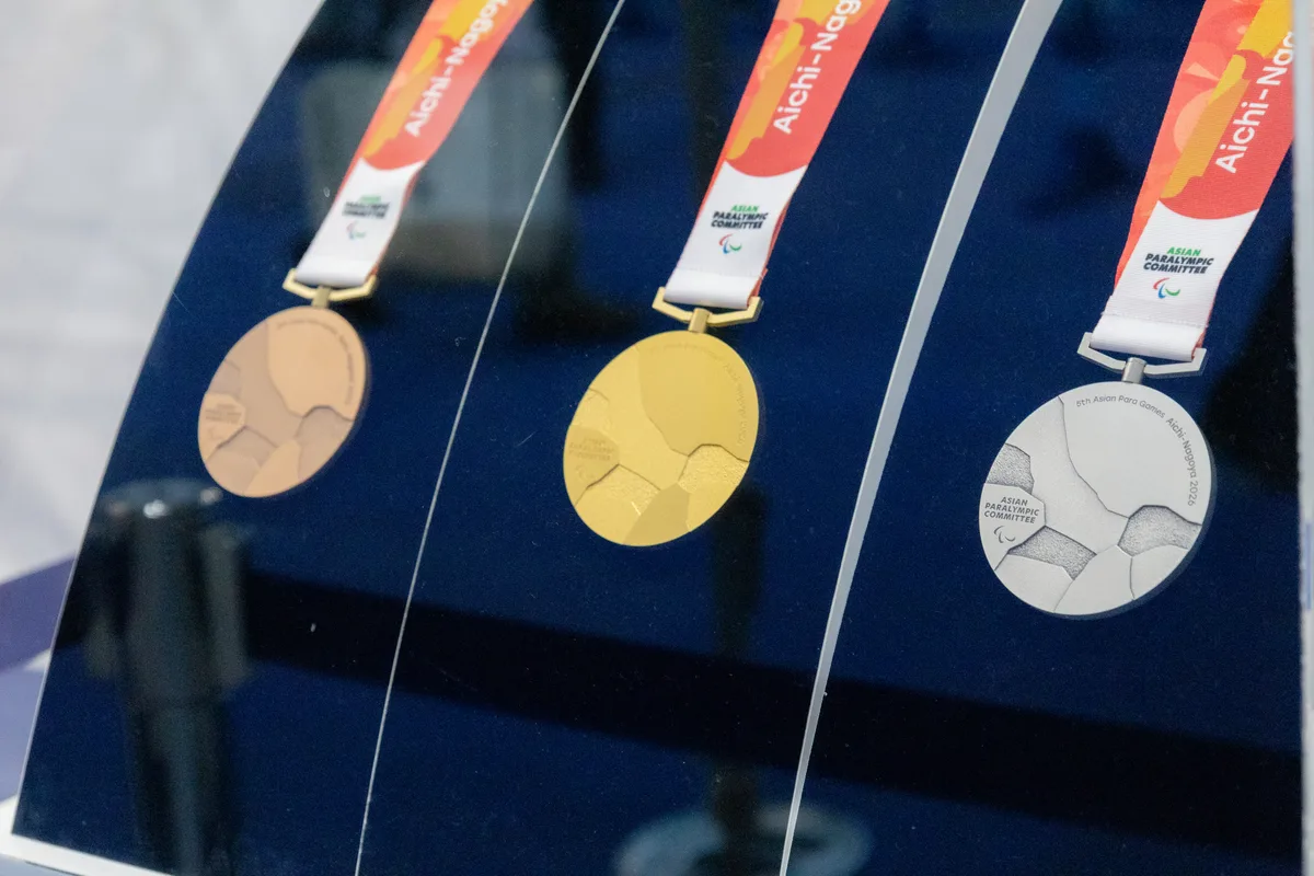 アジアパラ競技大会の金・銀・銅メダル。ガラスケースの中に、Aichi-Nagoya 2026 と書かれた赤いリボン付きで3つ並んでいる