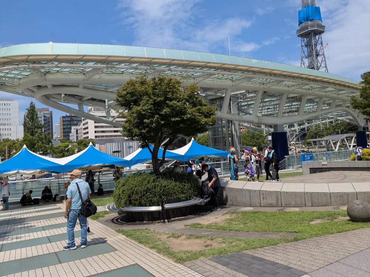 オアシス21 緑の大地から見上げた水の宇宙船のガラス屋根と青いテント、奥に中部電力MIRAI TOWER