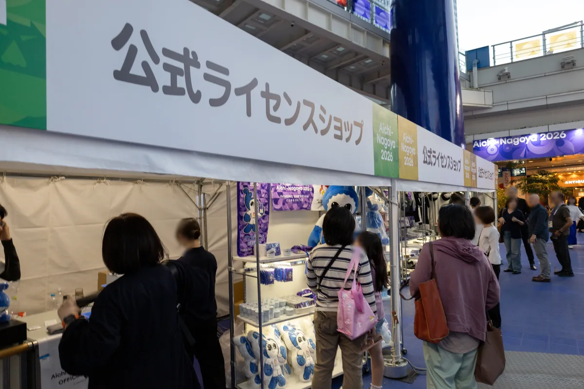 アジアパラ ライブサイトの公式ライセンスショップ。棚にウズミンのぬいぐるみやタオル、缶バッジなどが並び、買い物客が集まっている