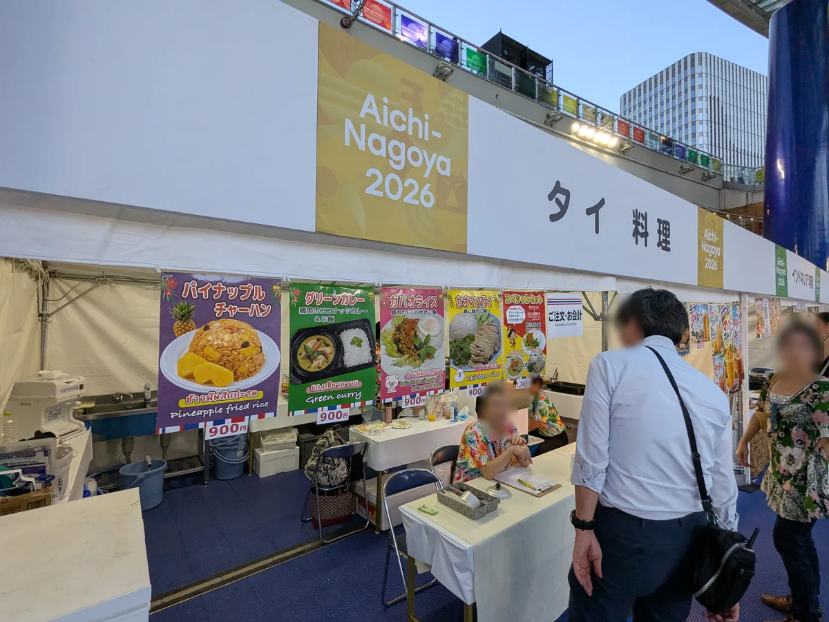 アジアパラ ライブサイトのタイ料理ブース。パイナップルチャーハン、グリーンカレー、ガパオライス、カオマンガイ各900円のメニューが掲示され、注文カウンターにスタッフが座っている