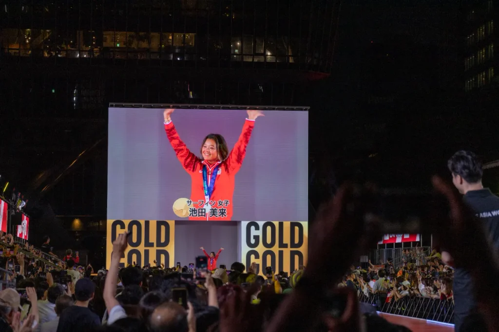 9月30日のメダリストセレブレーションで、大型ビジョンに映るサーフィン女子 金メダルの池田美来選手と、スマートフォンを掲げる観客