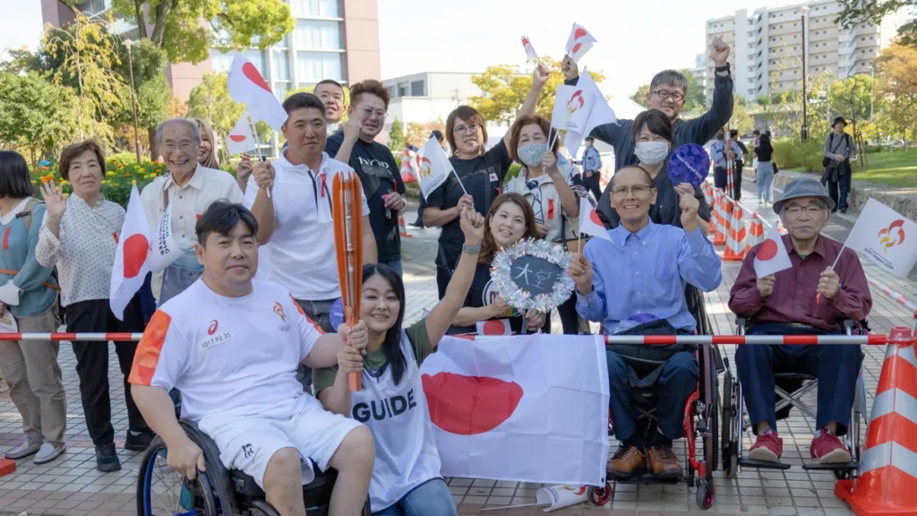 応援に駆けつけた家族や仲間と日の丸を掲げる大堂秀樹さん｜アジアパラ聖火リレー