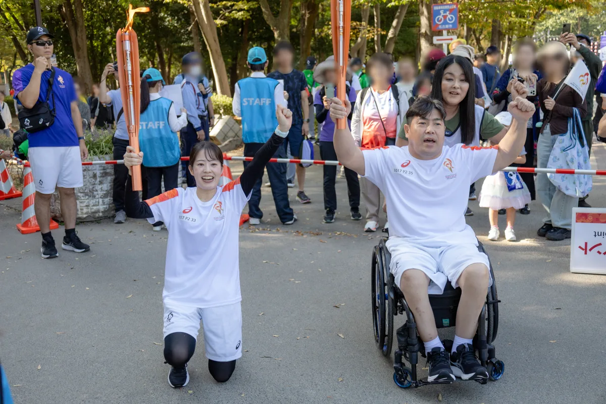 聖火を受け取り、前のランナーと2本のトーチを高く掲げる大堂秀樹さん