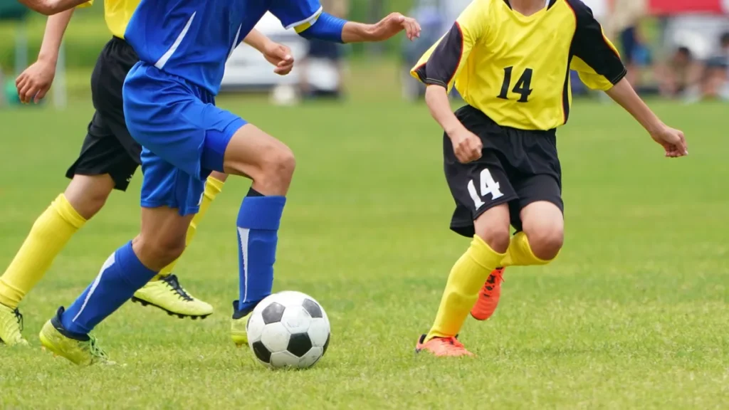 芝生のグラウンドでボールを追うサッカー選手たちの足元