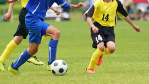 芝生のグラウンドでボールを追うサッカー選手たちの足元