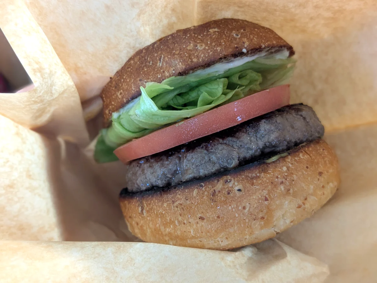 バーガー袋に入れたCHEDDARのクラシックバーガー。全粒粉入りのバンズにパティとトマト、レタスを挟んでいる