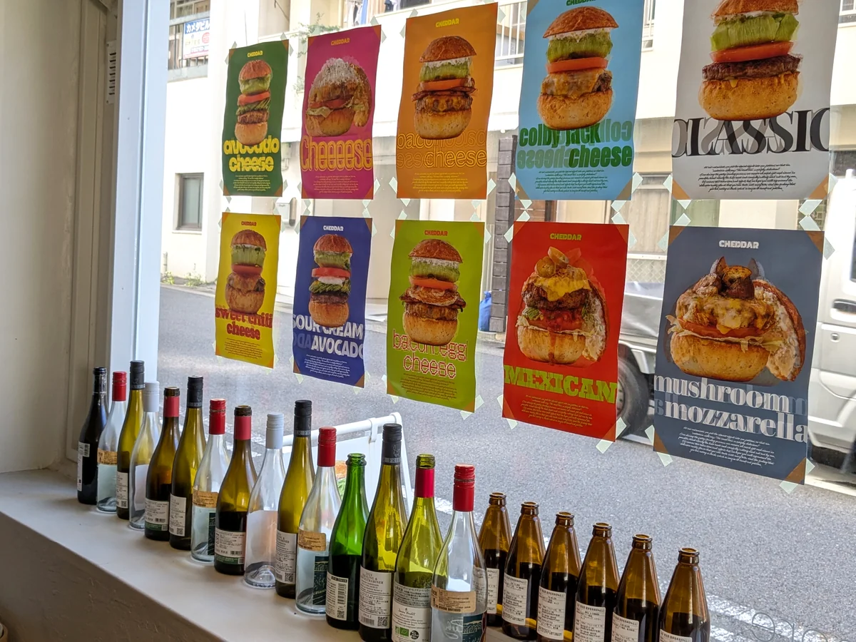 CHEDDARの窓辺に並ぶナチュールワインのボトルとハンバーガーのポスター