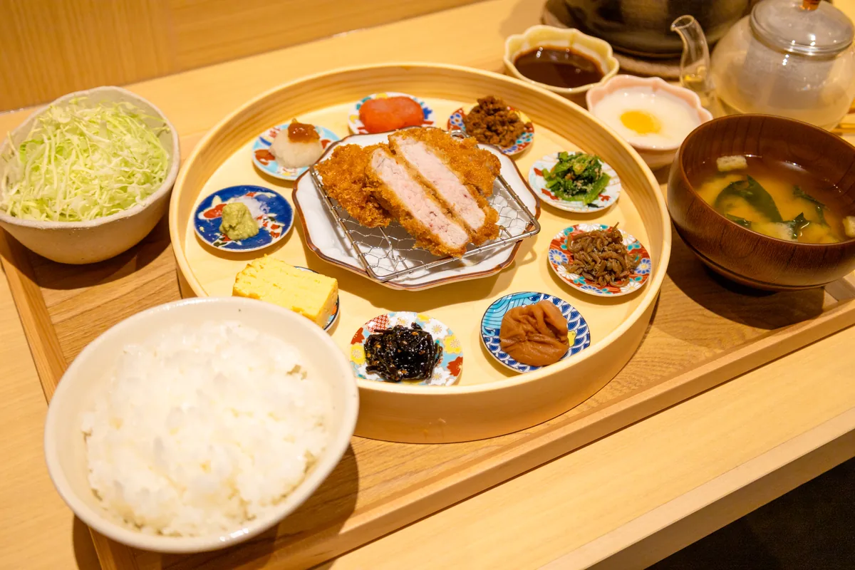夜限定の「華やぎロースかつ御膳」。ロースかつのまわりに9つの豆皿が並び、ごはん・味噌汁・キャベツ・卵黄をのせたとろろ・ソースが付く