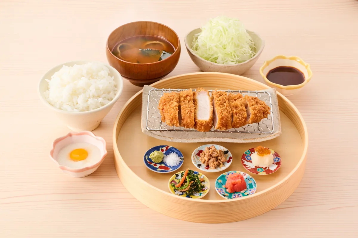 CHITAKAのロースかつ御膳〈豆皿仕立て〉。網にのったロースかつと5つの豆皿に、ごはん・味噌汁・キャベツ・卵黄をのせたとろろ・ソースが付く