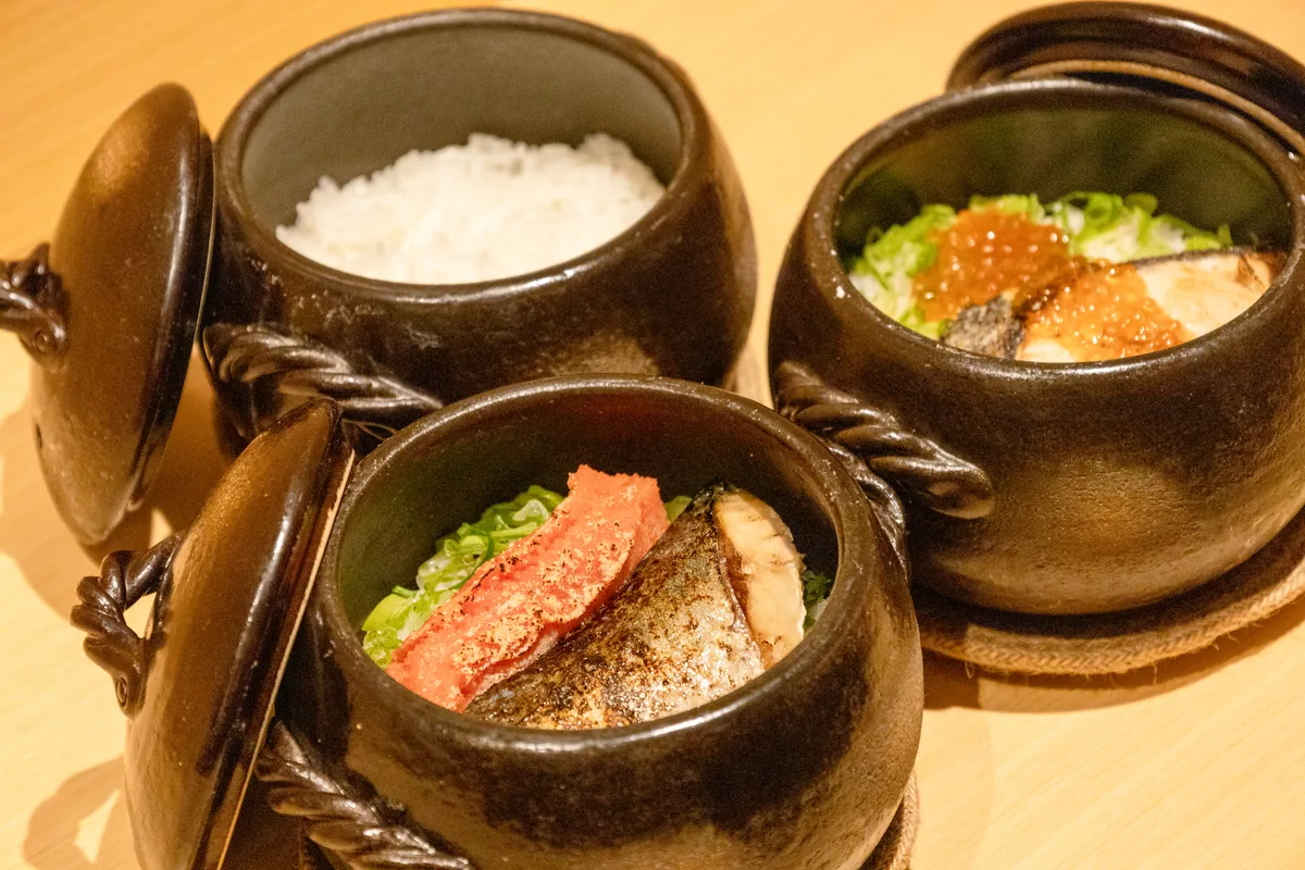 ふたを開けた1合炊きの小さな土鍋3つ。白いごはんのほか、焼き鯖と明太子をのせたもの、いくらをのせたものがある