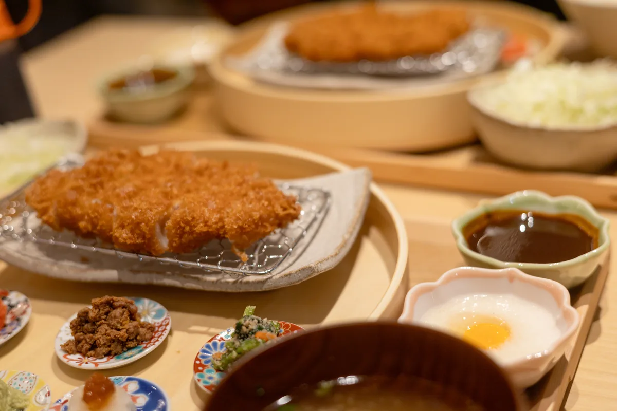 ロースかつと豆皿の横に、ソースと卵黄をのせたとろろ、味噌汁が並ぶ