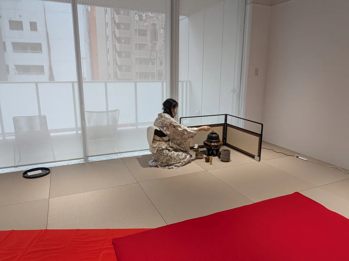 赤い毛氈が敷かれた畳の部屋で、屏風の前に座ってお点前をする表千家講師の鈴木貴子さん