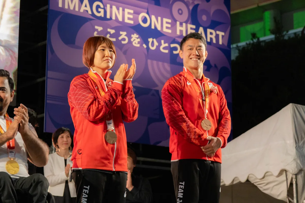 銅メダルを掛けてステージで拍手する藤原由衣選手と櫻井徹也選手