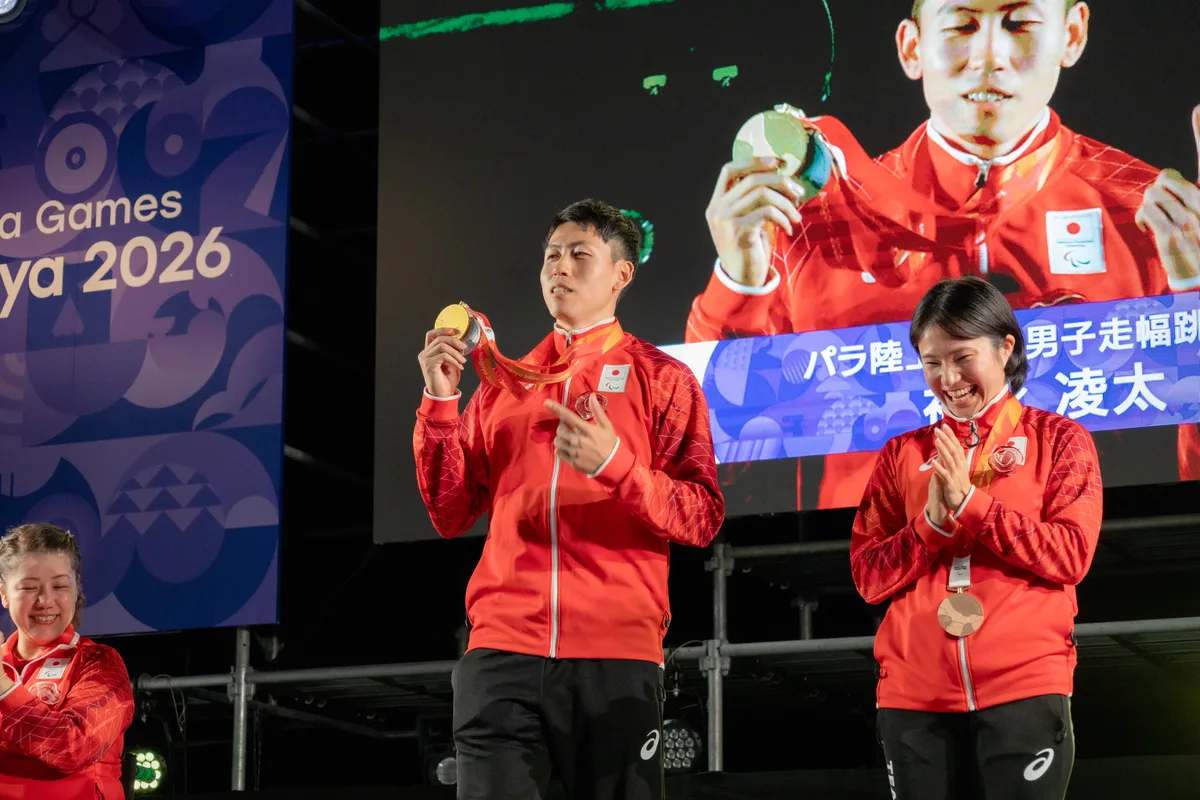 アスリートセレブレーションのステージで走り幅跳びの金メダルを掲げる福永凌太選手。右は拍手する加藤茜選手