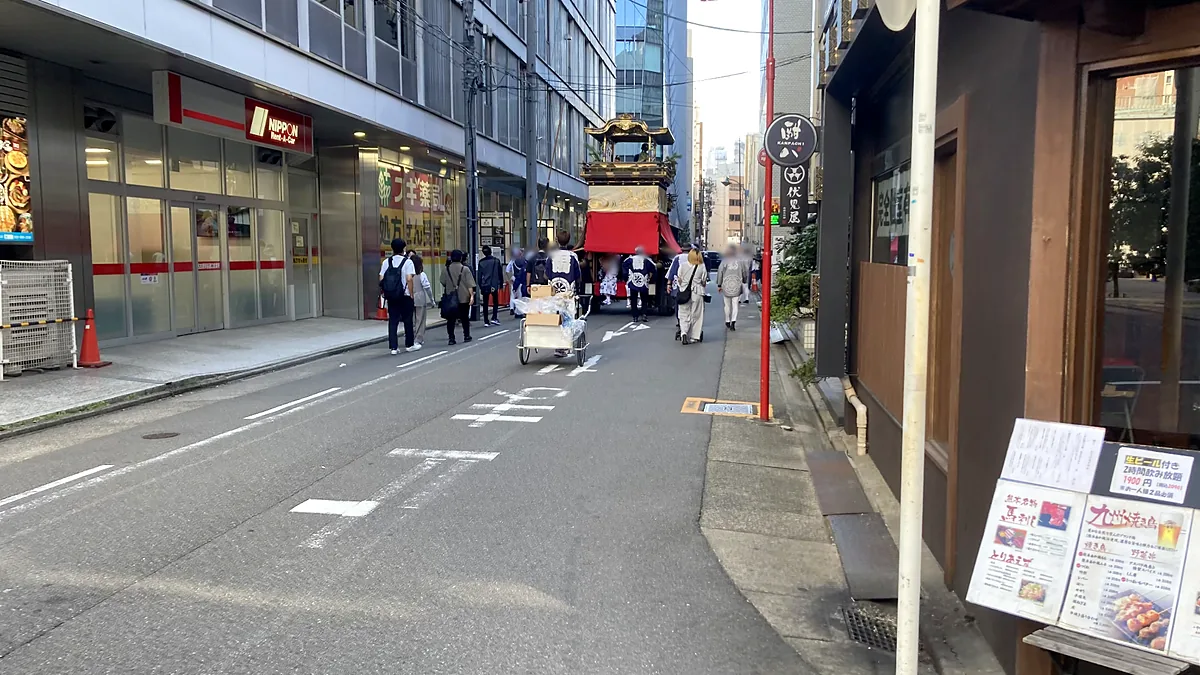 名駅のビル街の通りを進む二福神車と、法被姿の人たち