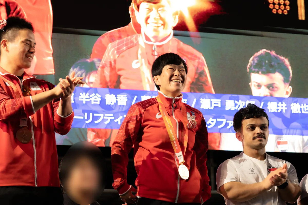 大型ビジョンを背に笑顔を見せる半谷静香選手。左に拍手する瀬戸勇次郎選手、右にイラクのムスリム・スダニ選手