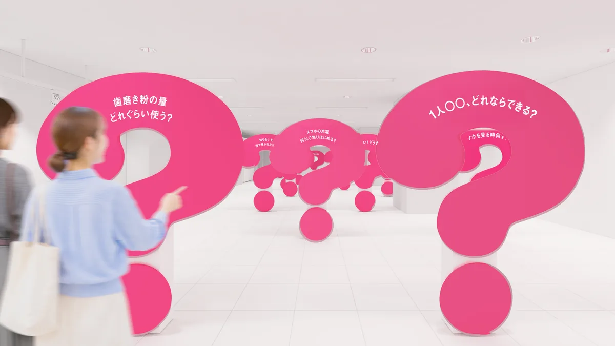はてな展のピンク色の展示室で「?」のオブジェを見る来場者