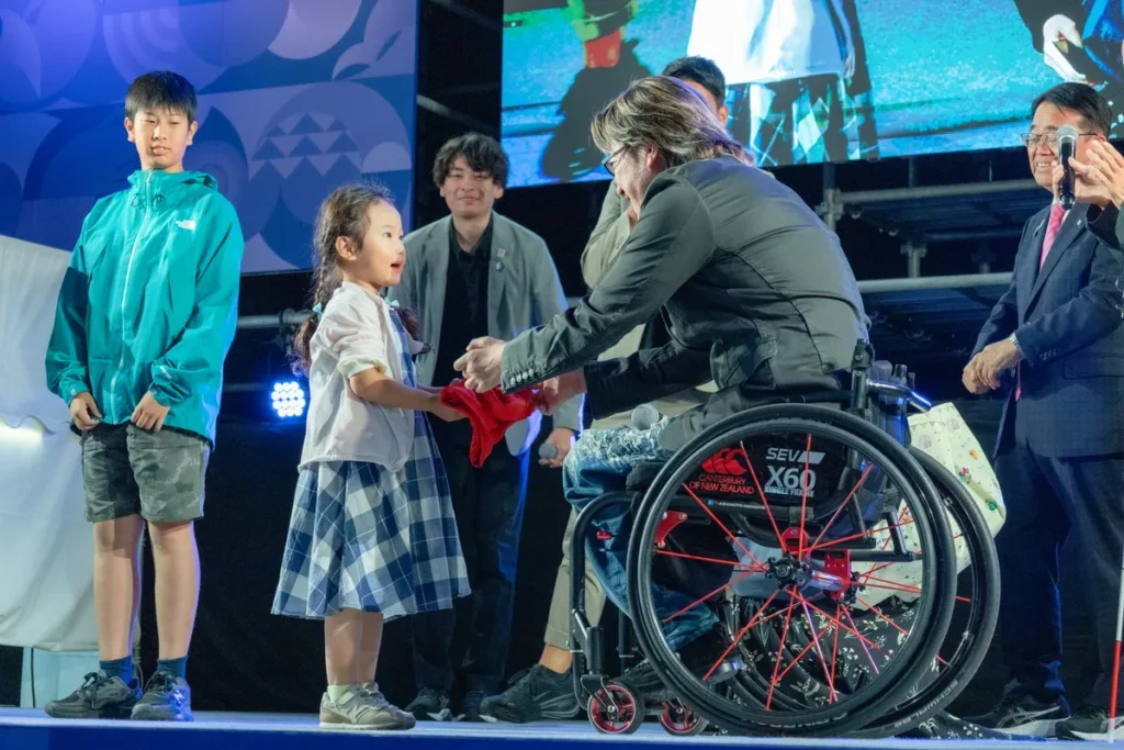客席から選ばれた子どもにサイン入りのウェアを手渡す池崎大輔さん