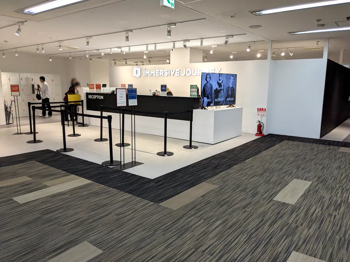 「IMMERSIVE JOURNEY」のロゴサインとRECEPTIONカウンター、モネ・モリゾ・ルノワールを映すモニター