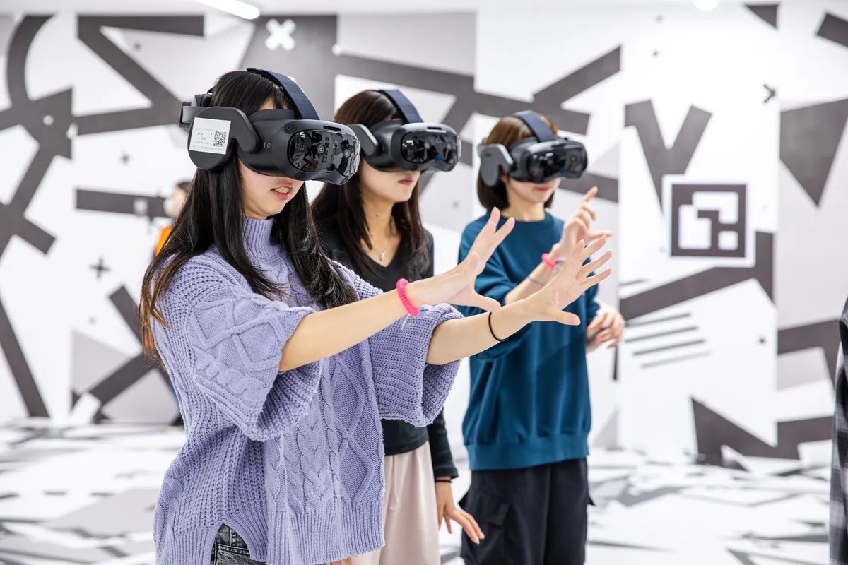 VRゴーグルを着けて両手を前に伸ばす3人。白と黒の模様で覆われたイマーシブジャーニー名古屋の体験エリア
