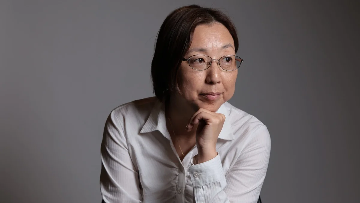 白いシャツ姿であごに手を当て、横を見る蓮見祥子さんのポートレート