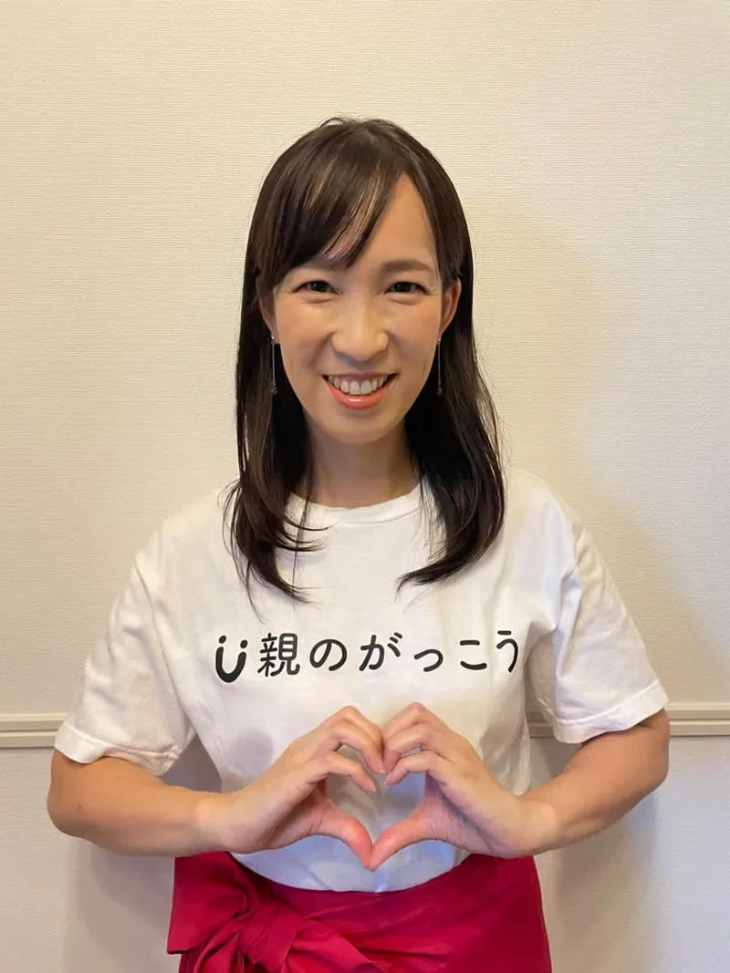 「親のがっこう」のTシャツを着て両手でハートをつくる上条厚子さん