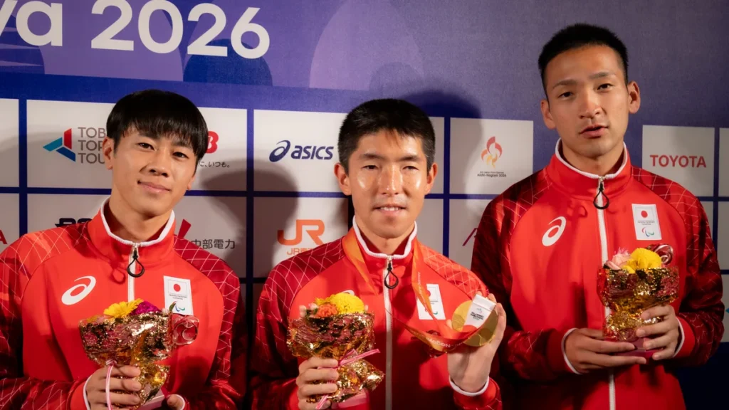 パラ陸上の唐澤剣也選手とガイドランナーの堀越翔斗さん・清水琢馬さん。金メダルと花束を手にミックスゾーンで