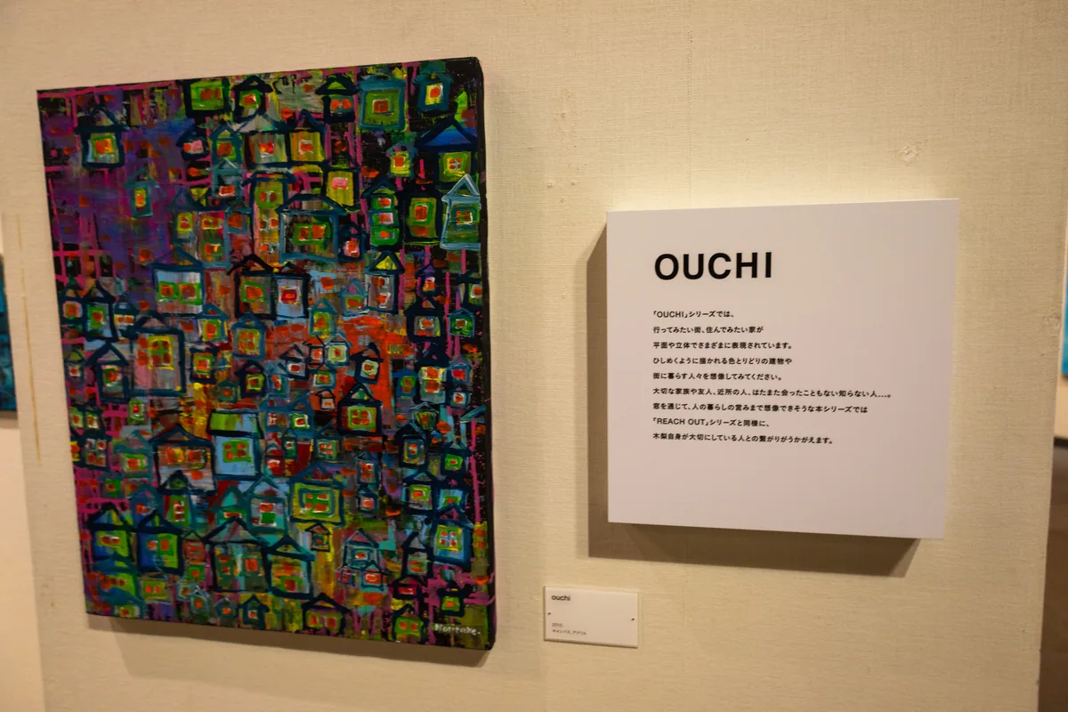 色とりどりの家がひしめくように描かれた木梨憲武さんの「OUCHI」シリーズの作品と説明パネル