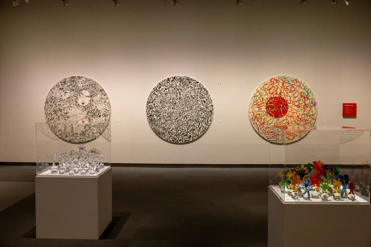 手のひらを描いた3点の大きな円形の作品と、手前のガラス作品が並ぶ木梨憲武展の「REACH OUT」コーナー