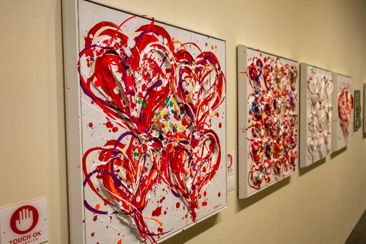 赤い絵の具を厚く盛り上げてハートを描いた木梨憲武さんの触れる作品と「TOUCH OK」のマーク