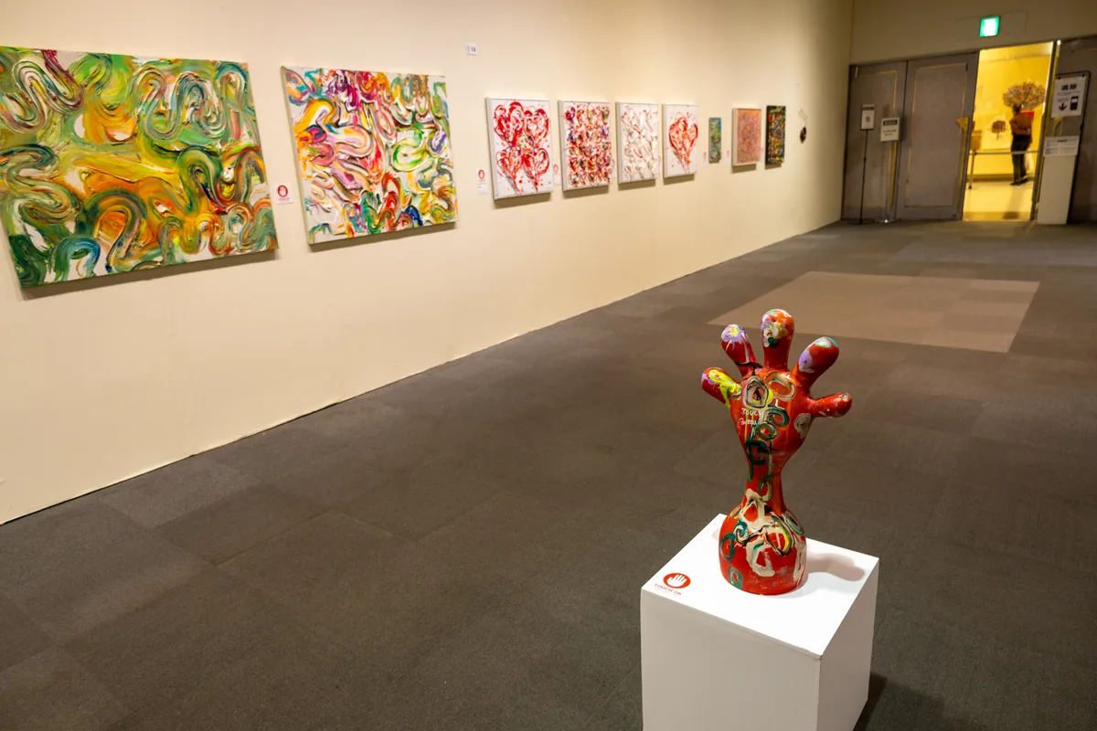 赤い手の形のオブジェが中央に置かれ、壁にカラフルな作品が並ぶ木梨憲武展の「TOUCH」のコーナー