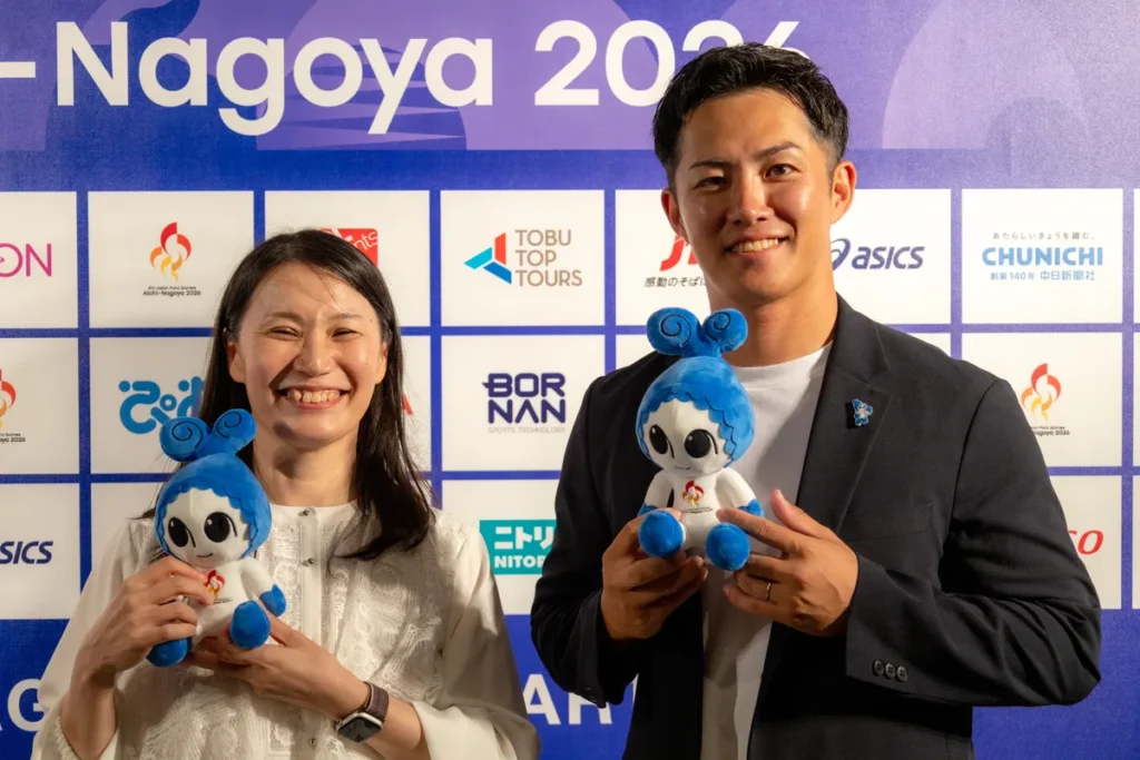 アジアパラ競技大会のマスコット「ウズミン」のぬいぐるみを手に笑う伊藤則子さんと小須田潤太さん