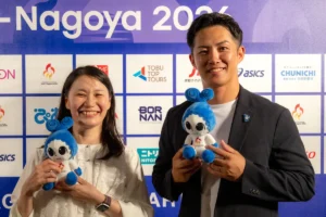 アジアパラ競技大会のマスコット「ウズミン」のぬいぐるみを手に笑う伊藤則子さんと小須田潤太さん